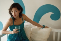 Woman sitting on daybed, holding water and looking at camera - Yukmin