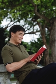 Man sitting on bench in park reading - Yukmin