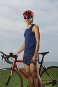Man standing next to bike along ocean, looking at camera, smiling - Yukmin