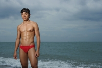 Muscled man wearing swim trunks by ocean, swimming - Yukmin