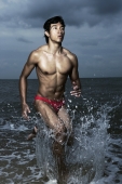 Muscled man wearing swim trunks, running out of ocean, triathlon, race - Yukmin