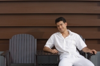 Young man sitting in garden chair and looking at camera - Yukmin