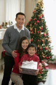 Young parents with boy present in hand at Christmas smiling at camera - Alex Mares-Manton