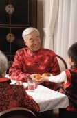 Boy presenting two mandarin oranges to grandfather at dinner table - Alex Mares-Manton