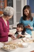 Grandmother, daughter and granddaughter making dumplings in the kitchen - Alex Mares-Manton