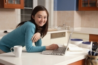 Young woman using laptop on kitchen top, looking at camera - Alex Mares-Manton