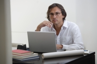 Businessman using laptop at the desk, looking at camera - Yukmin