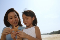 Mother and daughter at the beach, looking at shell - Yukmin