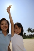 Mother with daughter holding up shell at the beach, smiling at camera - Yukmin