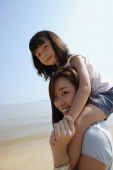 Mother carrying daughter on her shoulders at the beach, both looking at camera - Yukmin