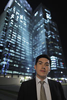 Man wearing a suit standing in front of lit buildings at night - Alex Mares-Manton