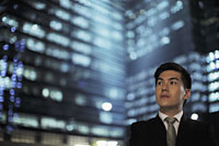 Man wearing a suit standing in front of lit buildings at night - Alex Mares-Manton