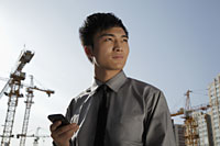 Young man holding phone, construction background - Alex Mares-Manton