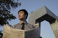 Young man holding a newspaper in front of the CCTV Building, Beijing, China - Alex Mares-Manton