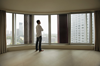 Rear view of young man looking out large windows of condo - Alex Mares-Manton