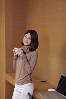 Young woman leaning against desk holding coffee - Alex Mares-Manton