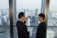 Two men talking in front of window with a view of the city of Beijing - Alex Mares-Manton