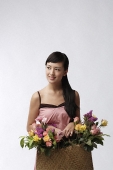 Young woman holding straw bag full of flowers - Asia Images Group