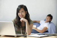 Young woman at computer, young man on couch - Asia Images Group