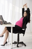 Profile of pregnant businesswoman at desk stretching - Asia Images Group