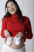 Pregnant woman holding baby shoes up to stomach - Asia Images Group