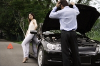 Man looking under car hood of broken down car, woman waiting - Asia Images Group