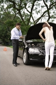 Woman looking under hood of car while man talks on phone - Asia Images Group