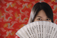 Chinese woman looking over hand-held fan with Chinese characters - Asia Images Group