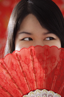 Chinese woman looking over hand-held fan - Asia Images Group