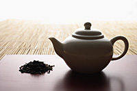 tea leaves in a pile and teapot on bamboo mat closeup - Asia Images Group