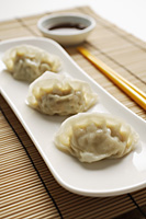 3 steamed gyoza dumplings placed on white plate with sauce on the side - Asia Images Group
