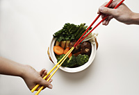hands holding chopsticks in clay pot of vegetables - Asia Images Group