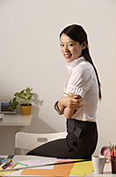 Chinese fashion designer sitting on desk, smiling at camera - Asia Images Group