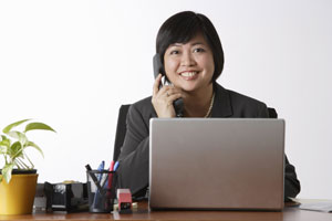 woman sitting at desk talking on phone - Asia Images Group