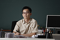man sitting at desk in front of chalk board - Asia Images Group