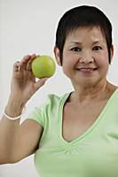 Mature Chinese woman holding green apple and smiling - Asia Images Group