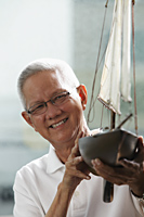 head shot of mature man holding model sail boat and smiling - Asia Images Group