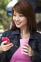 Young woman smiling holding a phone and drink - Asia Images Group