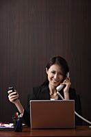 Young woman sitting at her desk holding her phones - Asia Images Group