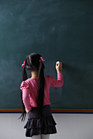 rear view of young girl with pony tails writing on chalkboard - Asia Images Group