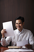 Man sitting at desk smiling at paper - Asia Images Group