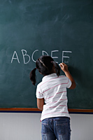 rear view of young girl writing on chalk board - Asia Images Group
