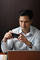 man sitting at desk looking phone - Asia Images Group