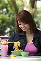 Young woman sitting outside eating noodles - Asia Images Group