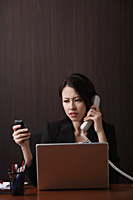 Woman sitting at her desk multi-tasking - Asia Images Group