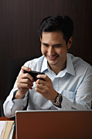man sitting at desk and looking at phone and smiling - Asia Images Group