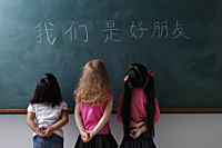 three young girls looking at Chinese characters "We are all friends" - Asia Images Group
