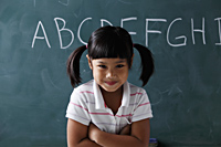 young girl with pony tails smiling in front of chalk board - Asia Images Group