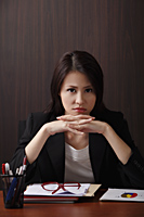 Woman sitting at desk with head on hands frowning - Asia Images Group