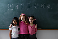 three young girls in front of chalk boards with Chinese writing "we are all friends." - Asia Images Group